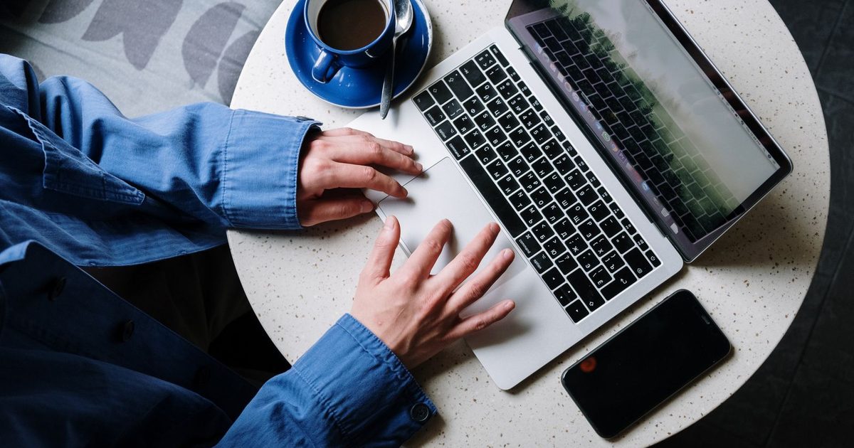 Dłonie na laptopie przy kawie w kawiarni, obok telefon