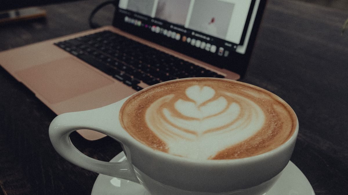 Filiżanka kawy z latte art przed otwartym laptopem w kawiarni