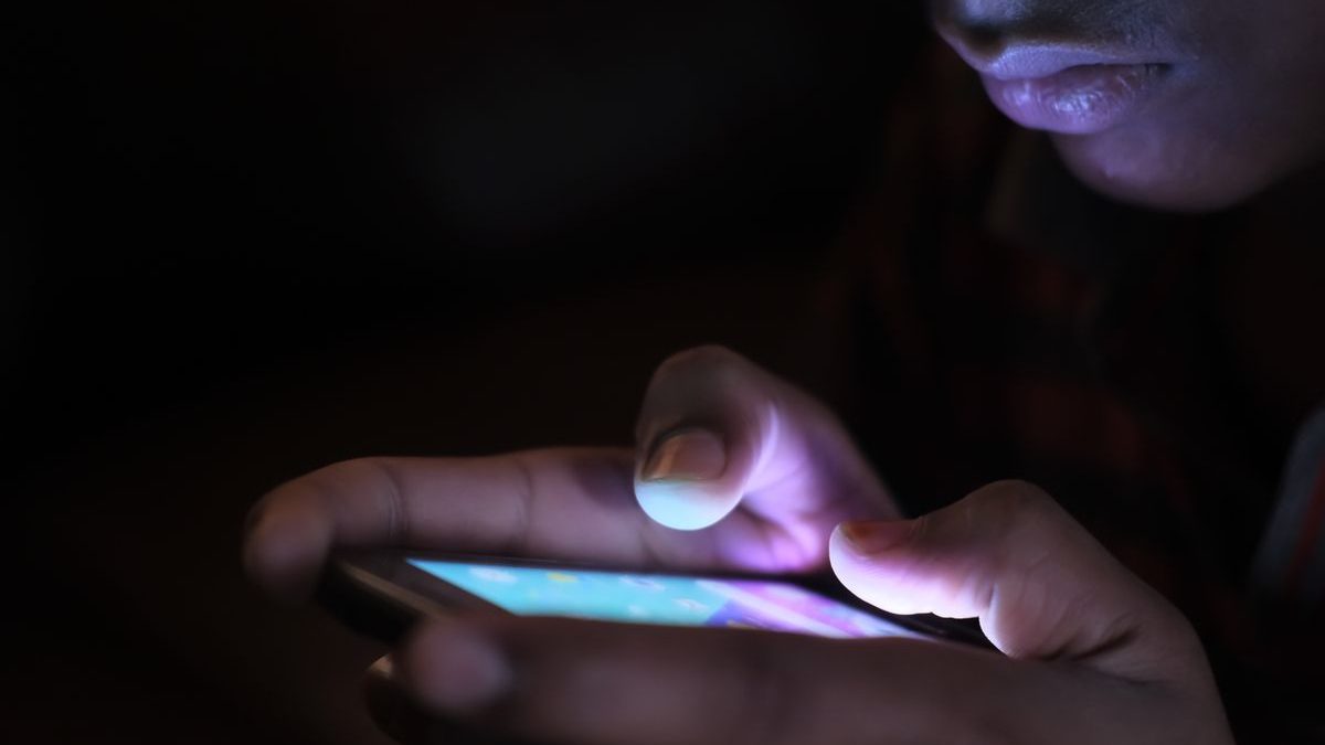 Dłonie trzymające świecący smartfon w ciemnym pokoju