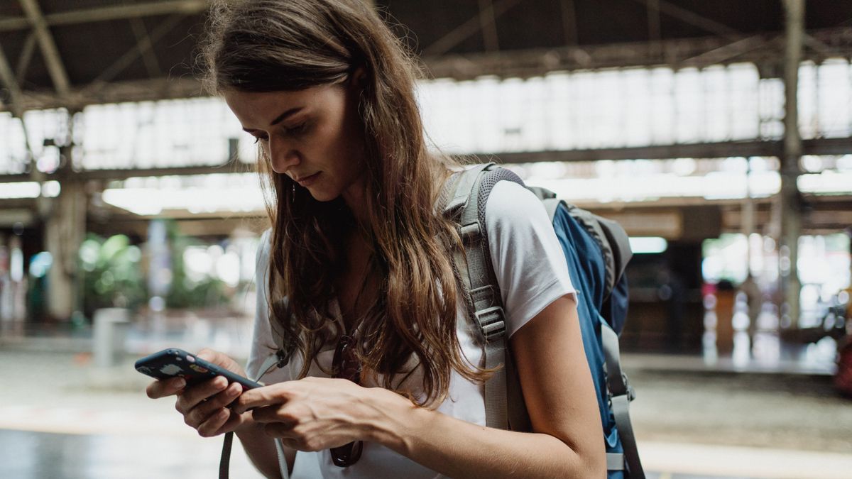 Kobieta z plecakiem sprawdza coś w telefonie na dworcu