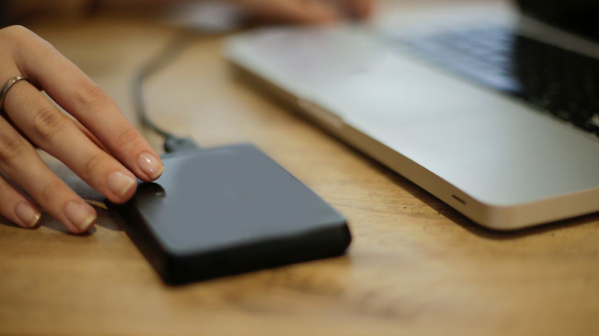 Dłoń na dysku zewnętrznym podłączonym do laptopa na drewnianym biurku