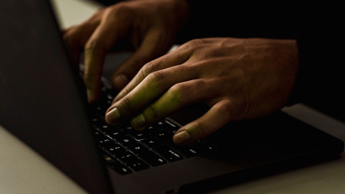 Dłonie piszą na klawiaturze laptopa w ciemnym pokoju