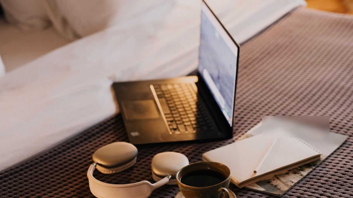 Laptop, słuchawki i kawa na hotelowym łóżku